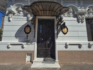 A building facade with a black ornate door, a decorative awning, and two signs indicating 'Chateau d'Ymau' and 'Corona Hotels.' - Chateau D'Amour Luxury Boutique (Bucharest)