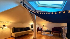 A cozy loft bedroom with a sloped ceiling, a sofa, two armchairs, a small table, and a skylight. - Chateau D'Amour Luxury Boutique (Bucharest)