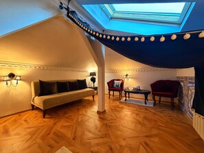 A cozy loft bedroom with a sloped ceiling, a sofa, two armchairs, a small table, and a skylight. - Chateau D'Amour Luxury Boutique (Bucharest)