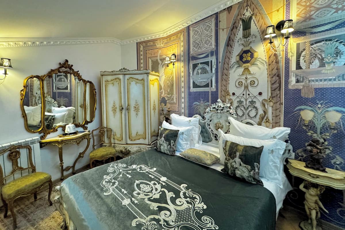 A room with a bed, a vanity with a mirror, a wardrobe, and a chandelier.