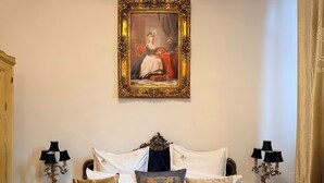 A bedroom with a bed, ornate headboard, decorative pillows, a framed painting, and two bedside tables with lamps. - Chateau D'Amour Luxury Boutique (Bucharest)