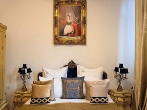 A bedroom with a bed, ornate headboard, decorative pillows, a framed painting, and two bedside tables with lamps. - Chateau D'Amour Luxury Boutique (Bucharest)