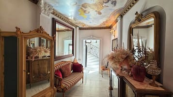 Un amplio pasillo con espejos ornamentados, un sofá lujoso y una escalera que conduce a un nivel superior.