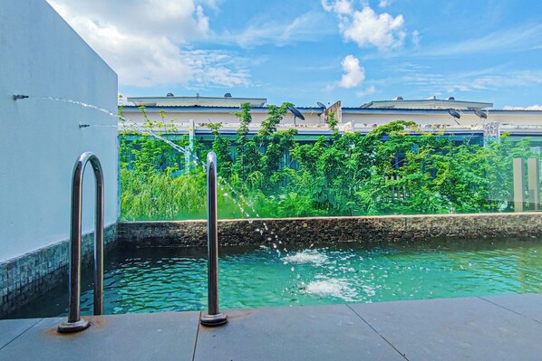 A pool with water jets, a metal railing, and a view of buildings and greenery.