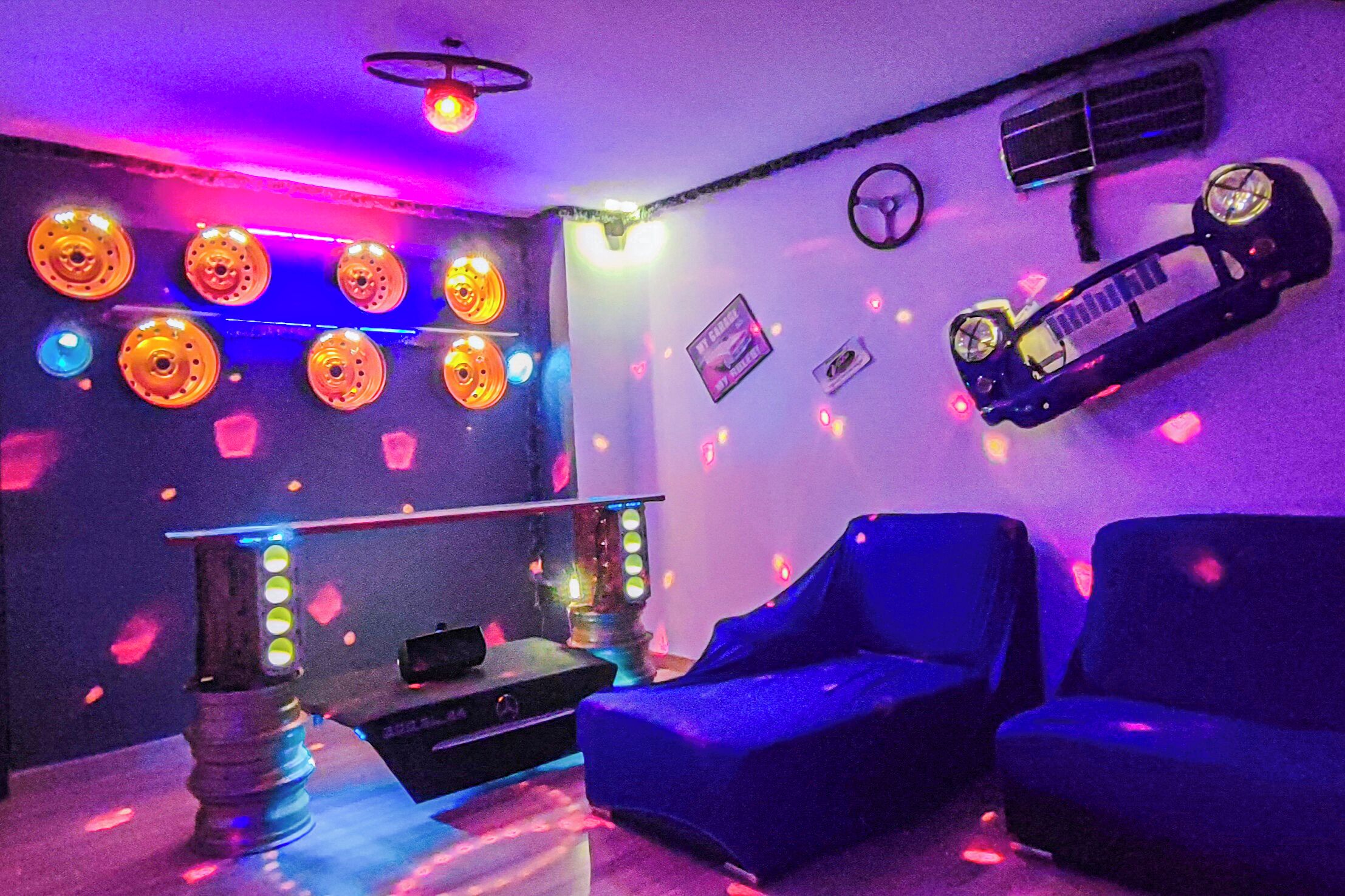 A room with a DJ setup, two blue chairs, and wall decorations including a poster and a clock.