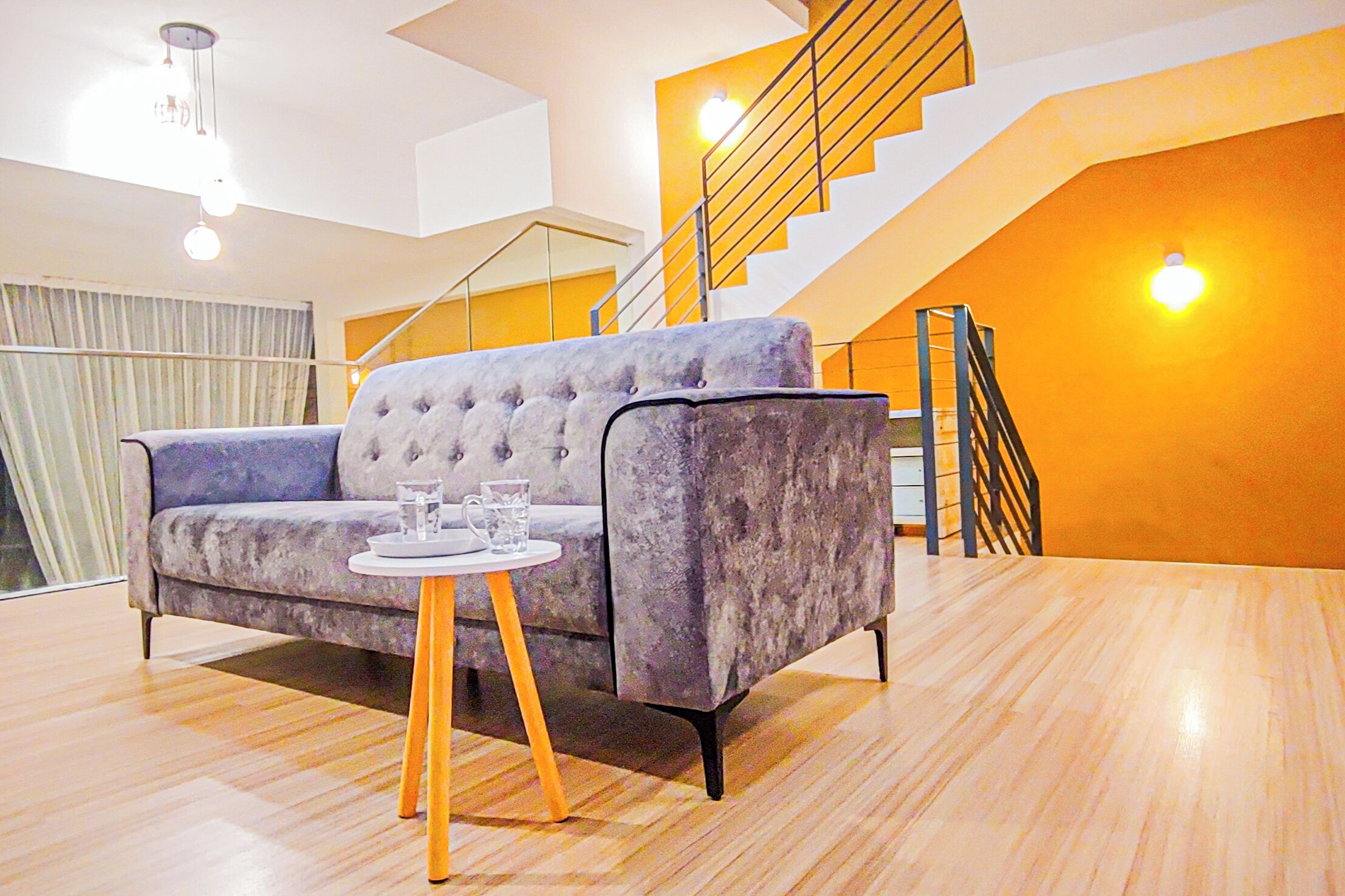 A modern living room with a sofa, a small round table, and a staircase with a yellow accent wall.
