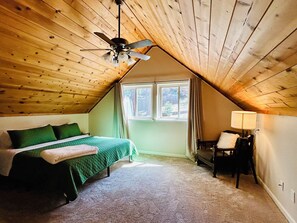 A bedroom with a sloped ceiling, a bed with green bedding, a nightstand, a chair, and a window. - Casa Montana - Charming 4-bedroom bungalow with AC in lovely Placerville (Chiang Mai District)