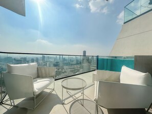 A balcony with white chairs and a round table, overlooking a cityscape with modern buildings. - Modern 1 Bedroom with Private Balcony Pool (Dubai)