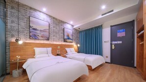 A hotel room with two beds, a brick wall, artwork, a wooden headboard, a blue curtain, and a door with a sign. - Qiqiaowu Hotel Songjiazhuang Station (Beijing)