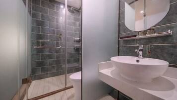 A modern bathroom with a glass shower enclosure, a white sink, and a mirror.