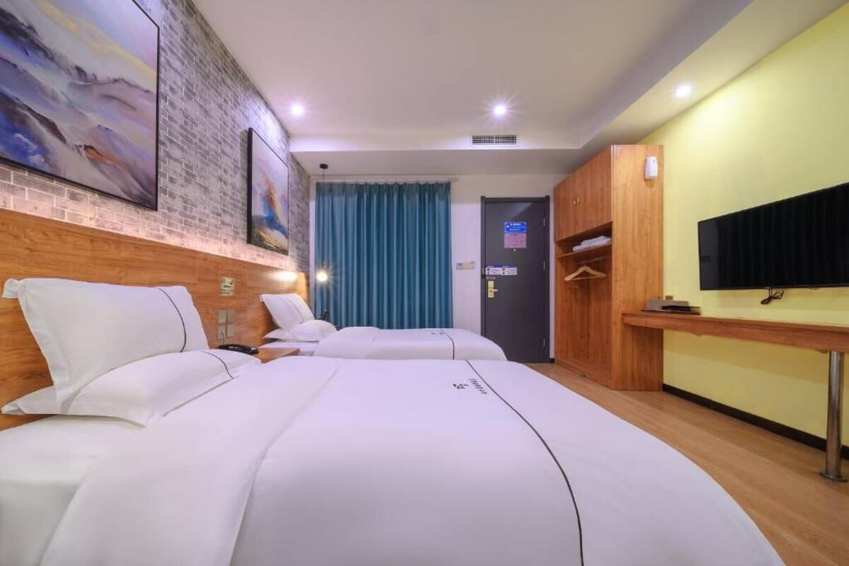 A hotel room with two beds, a flat-screen TV, a wooden wardrobe, and a painting on the wall.