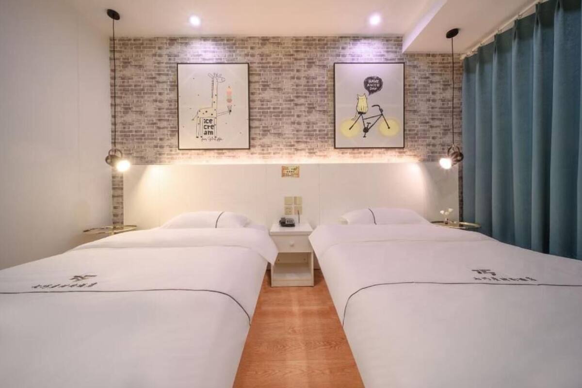 A hotel room with two beds, a brick wall, and two framed pictures.