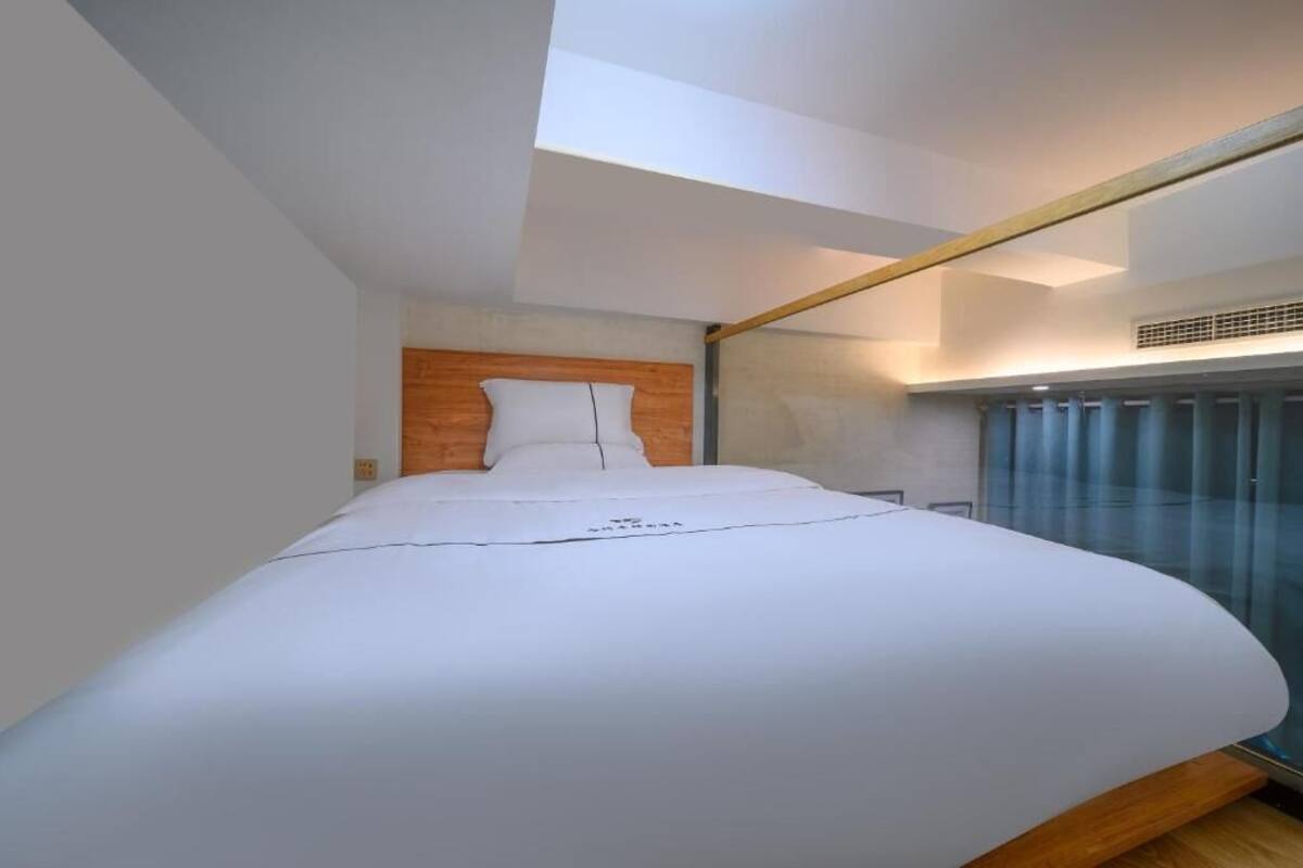 A modern bedroom with a large bed, a wooden headboard, and a skylight.