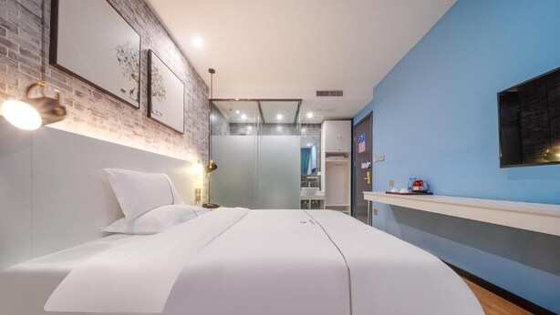 A modern hotel room with a large bed, a desk, a mirror, and a TV. - Qiqiaowu Hotel Songjiazhuang Station (Beijing)