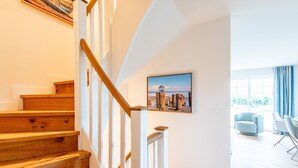 A staircase with wooden steps and white railings, a framed picture on the wall, and a modern living area with a sofa and chairs. - Sjipwai-Hüs 13c - Sjipwai-Hüs 13c in Westerland (Sylt)