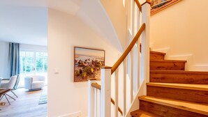 Un intérieur moderne avec un escalier en bois, un coin repas comprenant une table et des chaises, et une grande fenêtre.