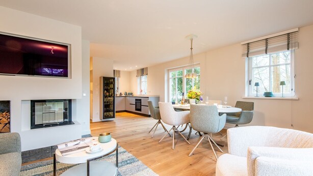 Un salon moderne avec une cheminée, un coin repas avec une table et des chaises, et une cuisine en arrière-plan.