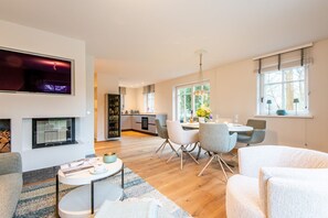 Uma sala de estar moderna com lareira, uma área de jantar com mesa e cadeiras, e uma cozinha ao fundo.
