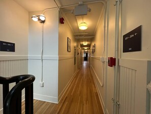 Un couloir d’hôtel avec un plancher en bois, des murs blancs et des panneaux de signalisation.