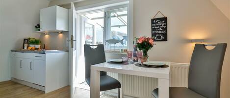 Une cuisine moderne avec des meubles blancs, une table à manger avec deux chaises et une fenêtre donnant sur l’extérieur.