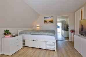 A bedroom with a bed, a bedside table with a plant, a wall-mounted light, and a painting.