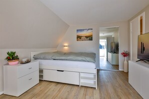 A bedroom with a bed, a bedside table with a plant, a wall-mounted light, and a painting.