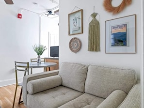 Ein Wohnzimmer mit einer Couch, einem runden Tisch mit Stühlen, Wandkunst aus Makramee und gerahmten Bildern.