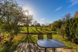 Eine Terrasse im Freien mit Tisch und Stühlen, umgeben von Bäumen und einer Wiese.