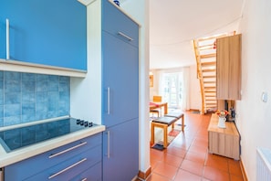 Eine kleine Küche mit blauen Schränken, einem Kochfeld aus Glas und einem Essbereich mit einem Holztisch und Stühlen.