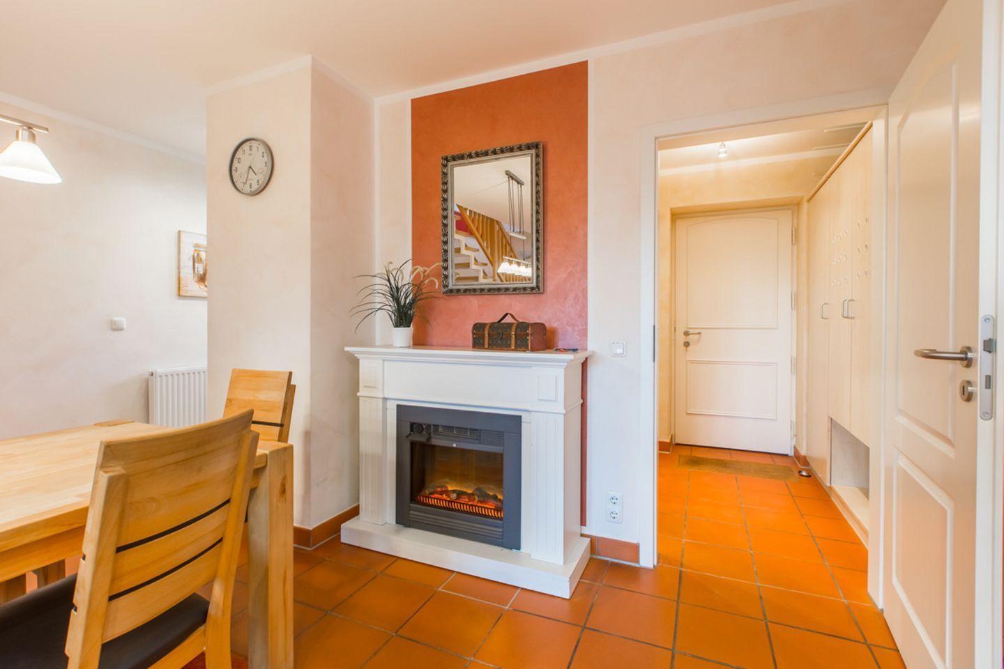 A dining area with a fireplace, a clock, and a door leading to another room.