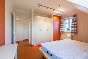 Ein Schlafzimmer mit Bett, Kleiderschrank, Tür und einem Fenster mit Vorhängen.