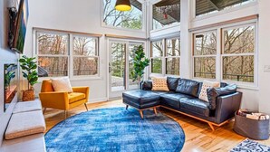 Ein geräumiges Wohnzimmer mit einem großen schwarzen Ledersofa, einem gelben Sessel und einem blauen Teppich.
