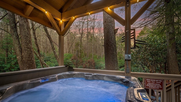 A hot tub under a wooden pergola with a forest view, surrounded by trees. - Riverfront Cabin | Sauna • Hot Tub • Private Trail (Cashiers)