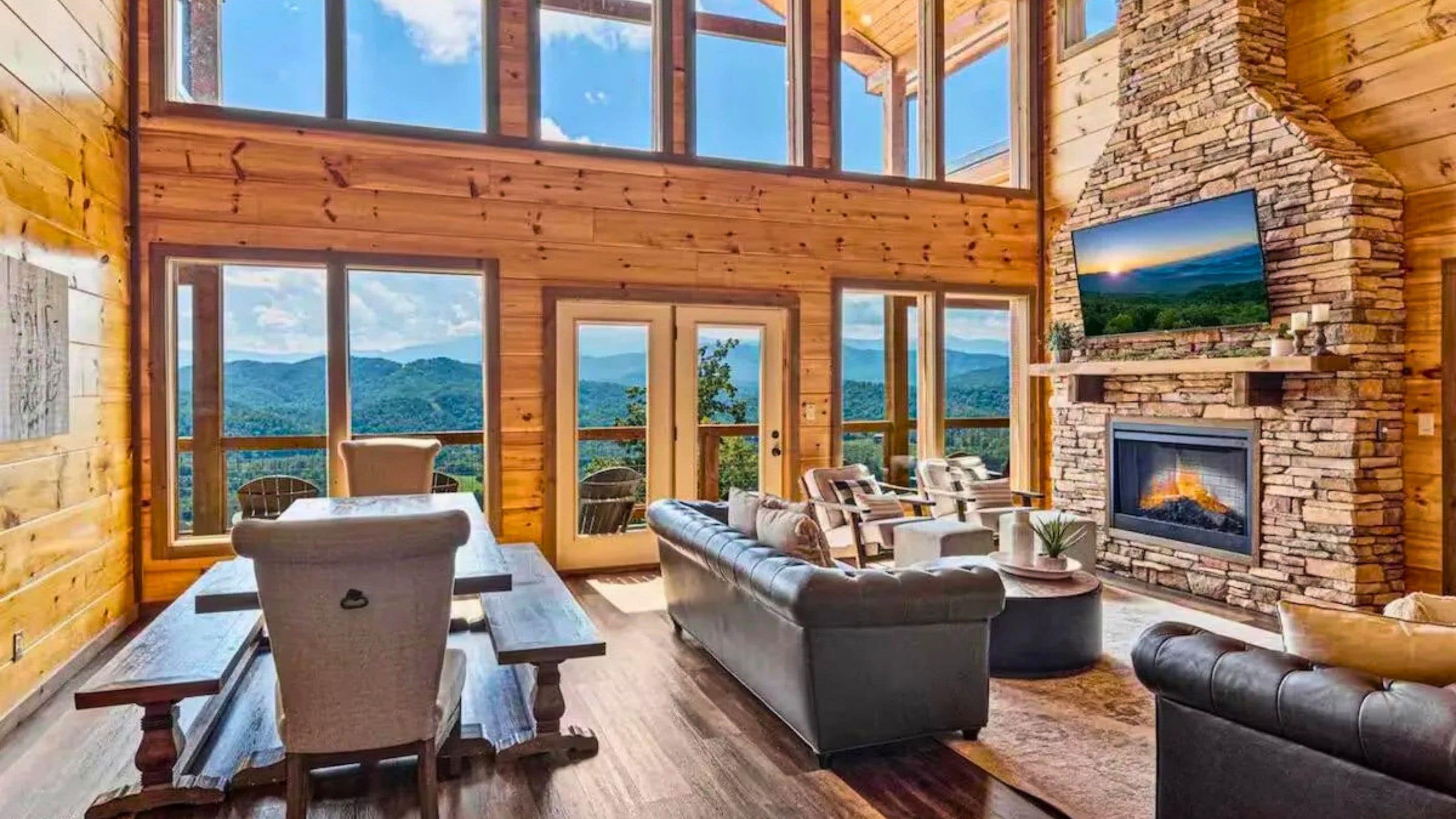 A spacious room with a stone fireplace, large windows offering mountain views, and a cozy seating area.