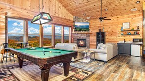 A cozy cabin interior with a pool table, a fireplace, a sofa, and a kitchen area. - Amazing Mountain Views | Indoor Pool | Game Room (Sevierville)