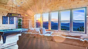 A wooden interior with a pool table, a sofa, and large windows offering a mountain view. - Amazing Mountain Views | Indoor Pool | Game Room (Sevierville)