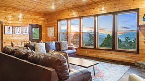 A cozy cabin interior with a leather sofa, wooden walls, and large windows offering mountain views. - Amazing Mountain Views | Indoor Pool | Game Room (Sevierville)