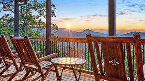 A wooden deck with a table and chairs, overlooking a mountainous landscape at sunset. - Amazing Mountain Views | Indoor Pool | Game Room (Sevierville)