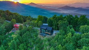 Una casa con un amplio balcón, rodeada de un bosque denso y montañas al fondo.