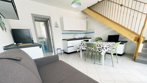 En stue med sofa, spisebord med stole, et køkken og en trappe.