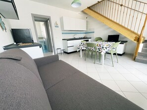 A living room with a sofa, a dining table with chairs, a kitchen area, and a staircase. - Seaside family flat with terrace-Beahost (Rosolina)