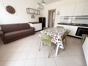A compact living space with a sofa, dining table, chairs, kitchenette, and a small refrigerator. - Seaside family flat with terrace-Beahost (Rosolina)