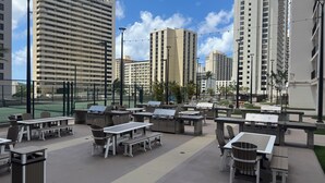 An outdoor patio area with tables and chairs, surrounded by high-rise buildings. - Waikiki Banyan with Free Parking & Washer/Dryer in Unit! (Honolulu)