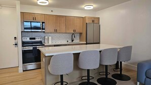 A modern kitchen with wooden cabinets, a stainless steel refrigerator, a built-in oven, and a bar area with four stools. - Waikiki Banyan with Free Parking & Washer/Dryer in Unit! (Honolulu)