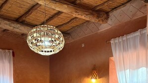 A bedroom with a large bed, a woven ceiling light, a wall-mounted lamp, and a small bedside table with a candle. - Tigmi Hamid (Assfalou)