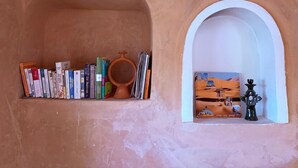 A shelf with books and a small painting in a rustic room. - Tigmi Hamid (Assfalou)