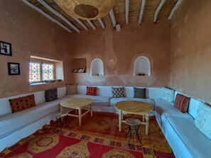 A room with a white sofa, two round wooden tables, a patterned rug, and a window with decorative bars.