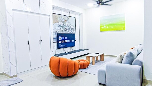 Een moderne woonkamer met een bank, een oranje poef, een televisie en kunst aan de muur.