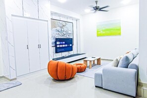 Una sala moderna con sofá, reposapiés naranja, televisor y obra de arte en la pared.