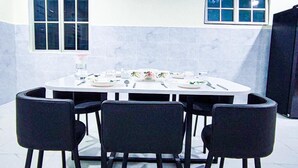 Een eetgedeelte met een ronde tafel, vier stoelen en een raam met zonwering.